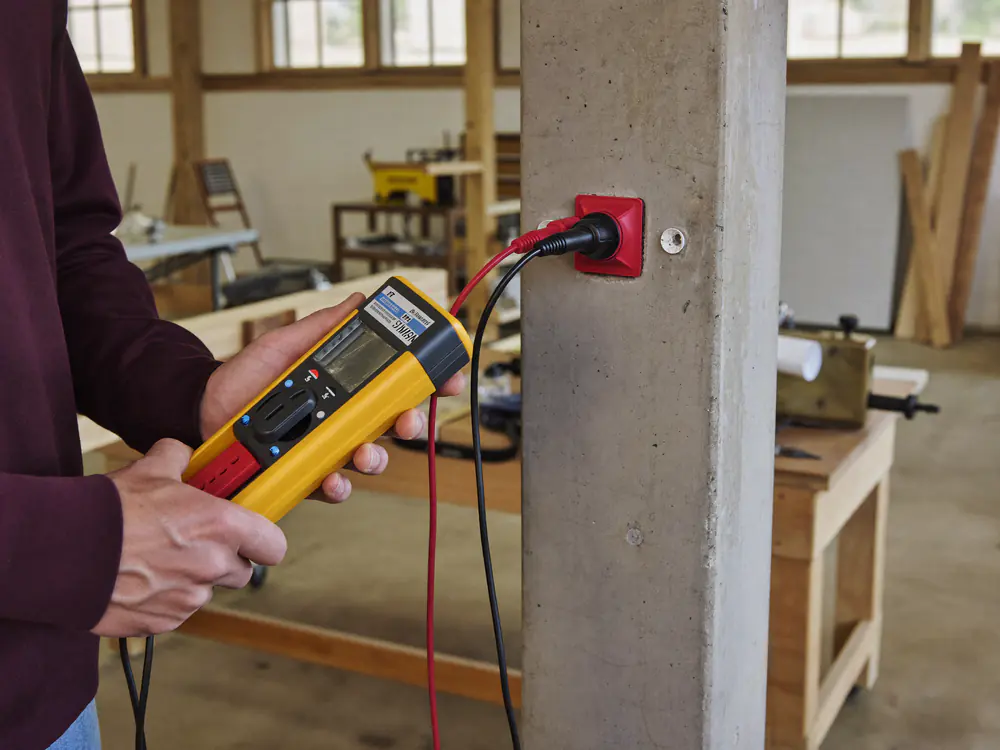 Installatietester aangesloten op een rood krachtstroomstopcontact in een timmerwerkplaats