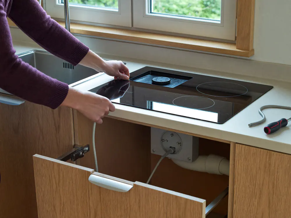 Handen sluiten een inductiekookplaat aan op de perilexaansluiting in het keukenkastje